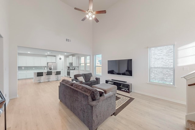 living room with light hardwood / wood-style flooring, ceiling fan, and a high ceiling