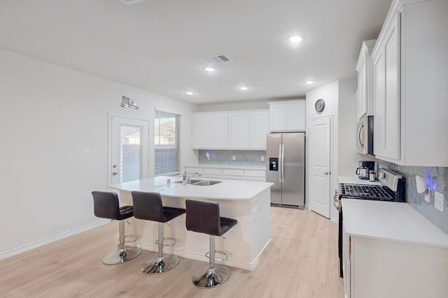 kitchen with appliances with stainless steel finishes, a breakfast bar, sink, white cabinets, and a kitchen island with sink