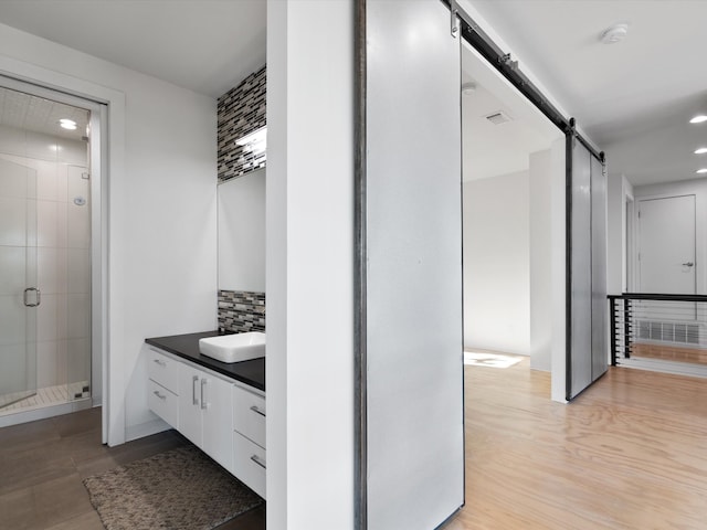 bathroom with vanity, a shower with door, hardwood / wood-style floors, and backsplash