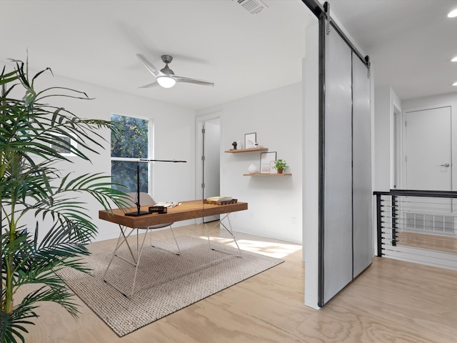 office space with a barn door, ceiling fan, and light wood-type flooring