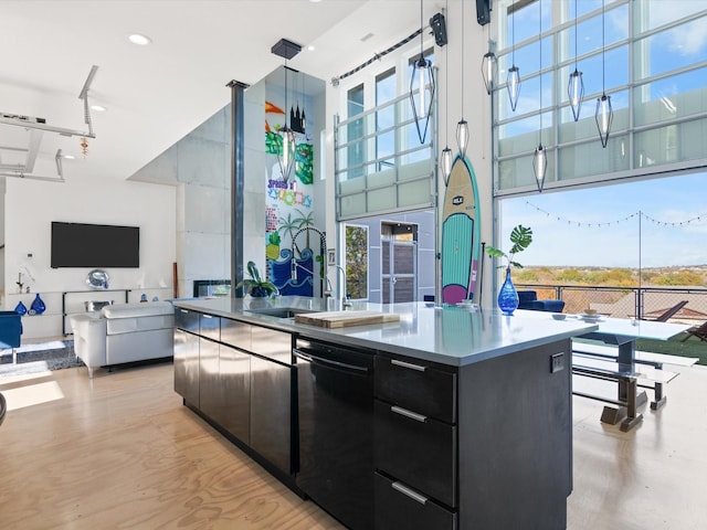 kitchen featuring dishwasher, a kitchen island with sink, a towering ceiling, plenty of natural light, and decorative light fixtures