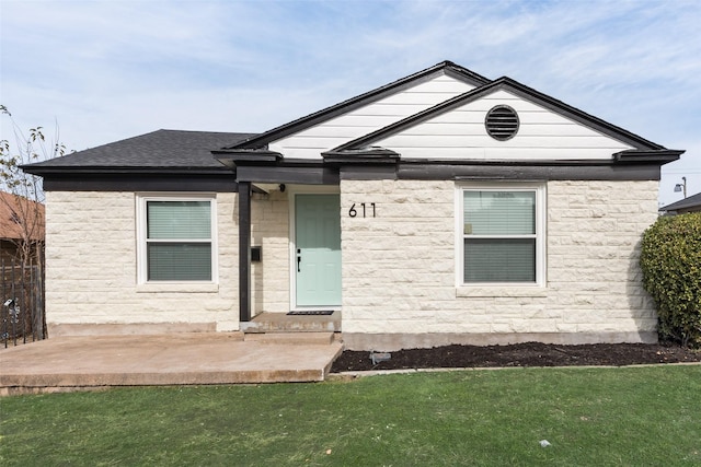 view of front of house with a shingled roof, a front yard, stone siding, and a patio area