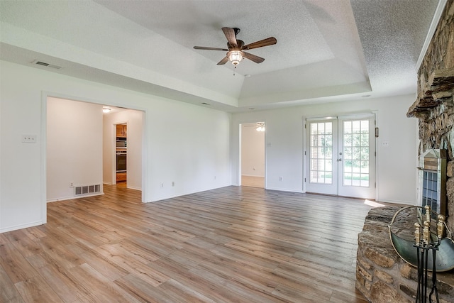 unfurnished living room featuring ceiling fan, a fireplace, light hardwood / wood-style floors, and french doors