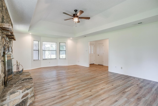 unfurnished living room featuring a stone fireplace, a textured ceiling, and light wood-type flooring