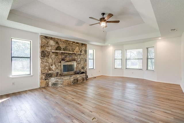 unfurnished living room with light hardwood / wood-style floors, a stone fireplace, plenty of natural light, and a tray ceiling