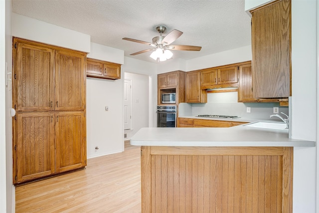 kitchen featuring kitchen peninsula, appliances with stainless steel finishes, ceiling fan, sink, and light hardwood / wood-style flooring