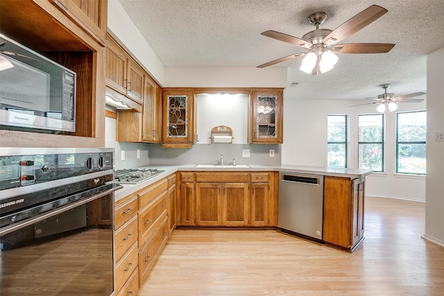 kitchen featuring sink, a textured ceiling, light hardwood / wood-style floors, kitchen peninsula, and stainless steel appliances