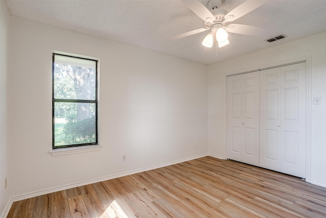 unfurnished bedroom featuring ceiling fan, a closet, a textured ceiling, and light wood-type flooring