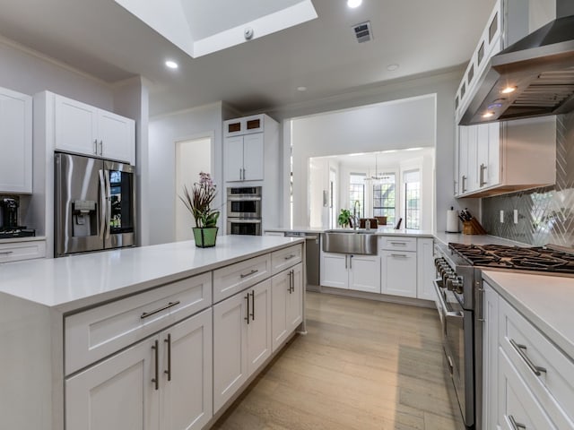 kitchen featuring wall chimney exhaust hood, white cabinetry, appliances with stainless steel finishes, and tasteful backsplash