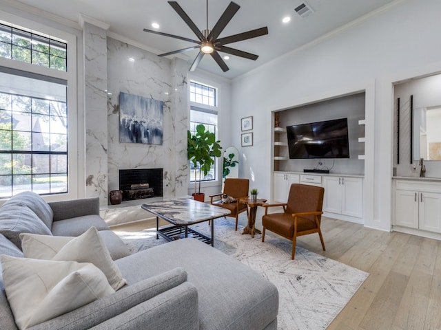 living room featuring sink, ceiling fan, light wood-type flooring, a fireplace, and ornamental molding