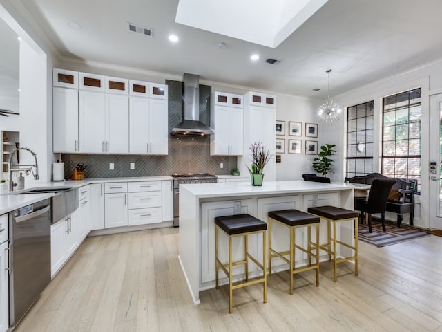 kitchen featuring a skylight, wall chimney exhaust hood, a kitchen island, white cabinets, and appliances with stainless steel finishes