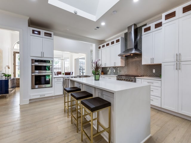 kitchen with white cabinets, appliances with stainless steel finishes, a center island, and wall chimney range hood