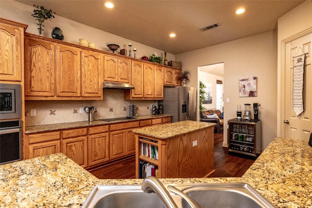 kitchen featuring dark wood-type flooring, light stone counters, tasteful backsplash, appliances with stainless steel finishes, and a kitchen island