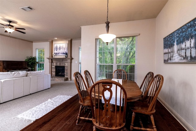 dining space with crown molding, a brick fireplace, dark wood-type flooring, and ceiling fan