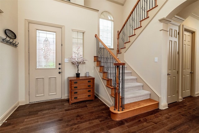 entryway with dark wood-style floors, arched walkways, stairway, and baseboards