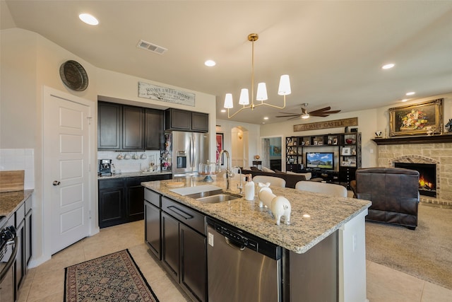 kitchen featuring pendant lighting, a center island with sink, a stone fireplace, sink, and appliances with stainless steel finishes