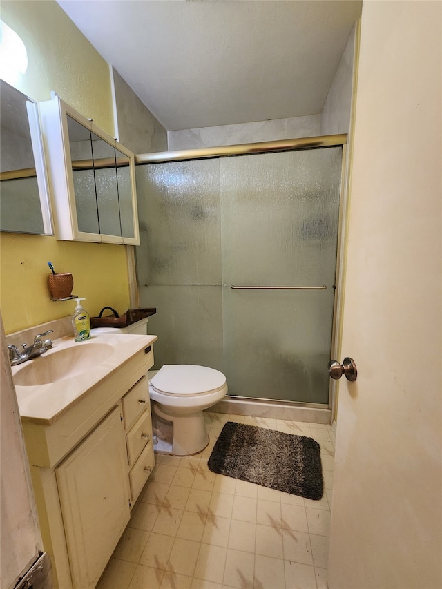 bathroom with tile patterned floors, a shower with door, vanity, and toilet