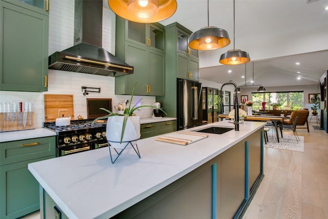 kitchen featuring wall chimney exhaust hood, green cabinets, hanging light fixtures, and vaulted ceiling