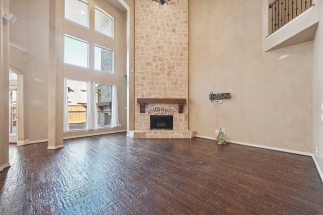 unfurnished living room with a stone fireplace, a towering ceiling, and dark wood-type flooring