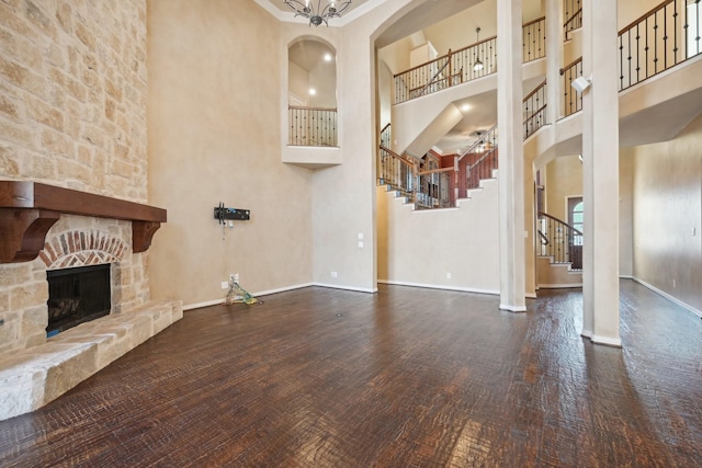 unfurnished living room with dark hardwood / wood-style flooring, a stone fireplace, and a towering ceiling