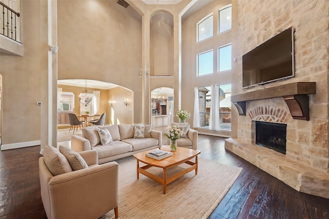 living room featuring a fireplace, dark wood-type flooring, a high ceiling, and an inviting chandelier