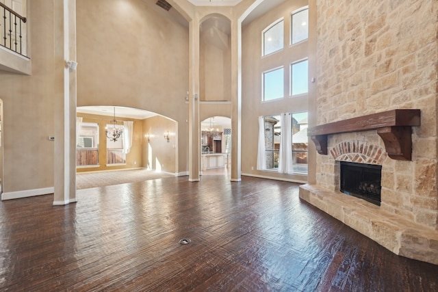 living room featuring hardwood / wood-style flooring, a stone fireplace, a towering ceiling, and a chandelier