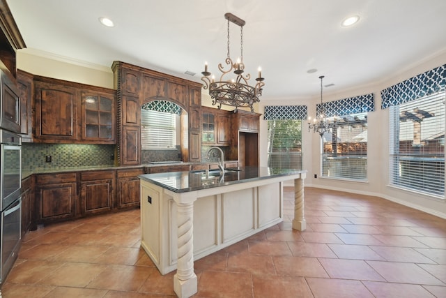 kitchen featuring decorative backsplash, a kitchen island with sink, a healthy amount of sunlight, and sink