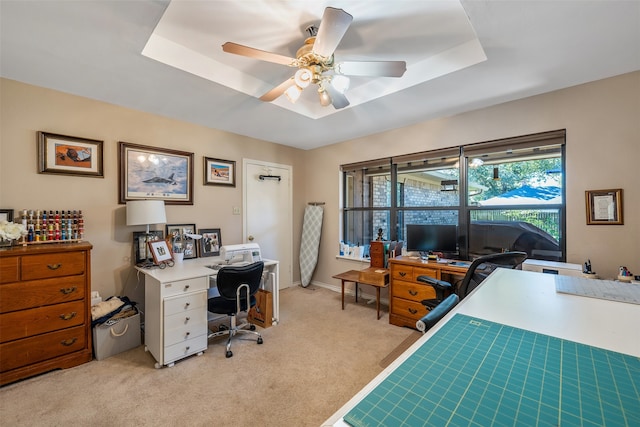 carpeted home office with a raised ceiling and ceiling fan