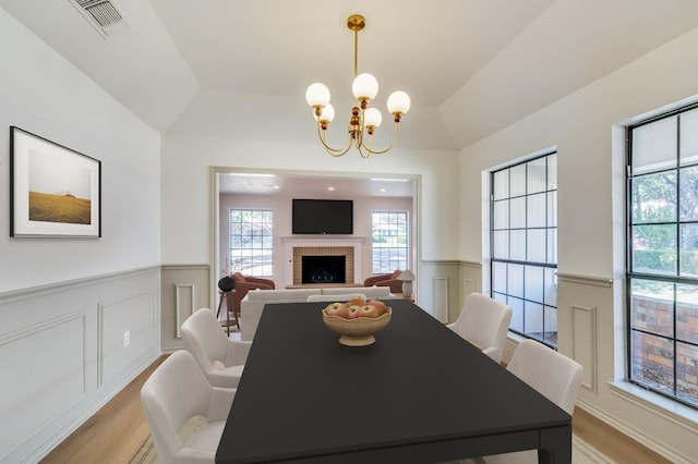 dining area featuring light wood-type flooring, an inviting chandelier, vaulted ceiling, and a fireplace