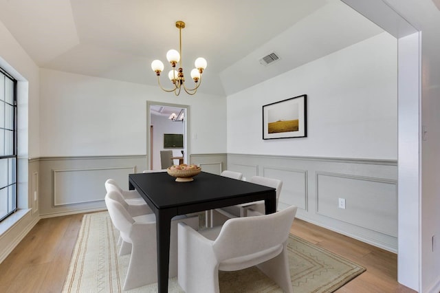 dining area featuring vaulted ceiling, light hardwood / wood-style floors, and a notable chandelier