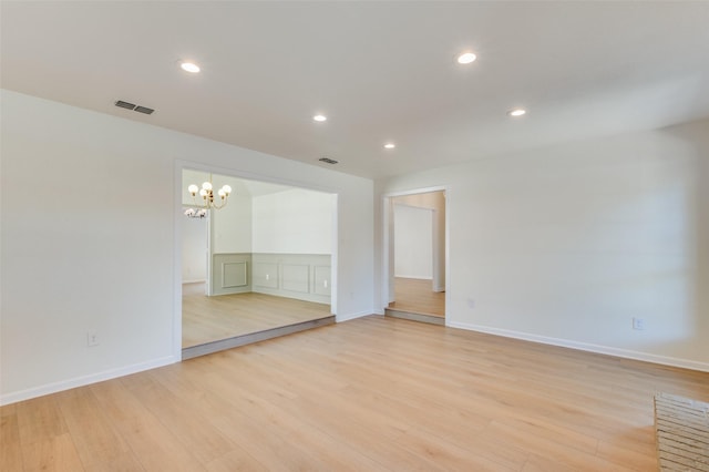 spare room featuring an inviting chandelier and light hardwood / wood-style flooring