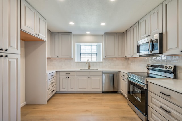 kitchen with stainless steel appliances, decorative backsplash, sink, and light hardwood / wood-style floors