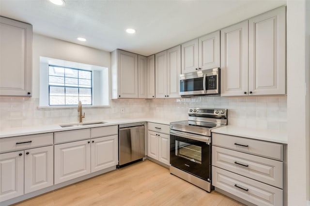 kitchen with appliances with stainless steel finishes, light wood-type flooring, backsplash, and sink