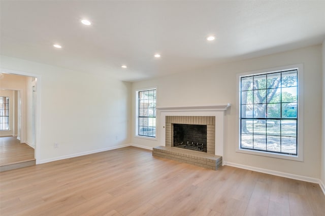 unfurnished living room with a brick fireplace, light hardwood / wood-style floors, and plenty of natural light