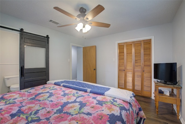 bedroom with ensuite bath, dark hardwood / wood-style floors, a closet, ceiling fan, and a barn door