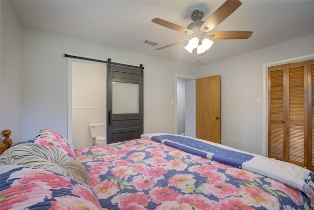 bedroom with ceiling fan, a barn door, and ensuite bath