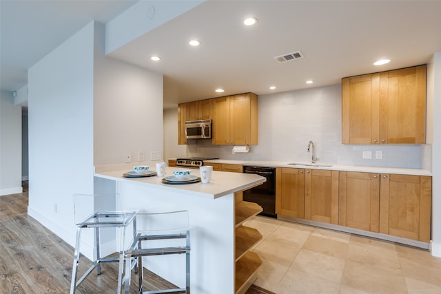 kitchen featuring sink, stainless steel appliances, tasteful backsplash, kitchen peninsula, and light wood-type flooring