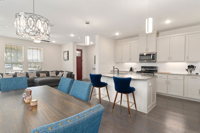 kitchen featuring a center island with sink, white cabinets, light stone countertops, appliances with stainless steel finishes, and dark hardwood / wood-style flooring