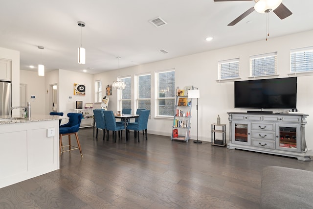 living room with ceiling fan with notable chandelier, dark wood-type flooring, and sink