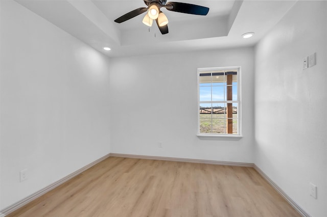 empty room featuring ceiling fan, a tray ceiling, and light hardwood / wood-style floors