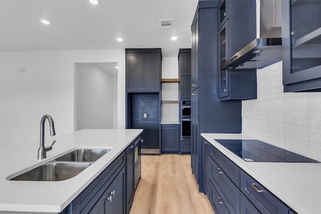 kitchen with sink, decorative backsplash, black electric cooktop, light wood-type flooring, and wall chimney exhaust hood