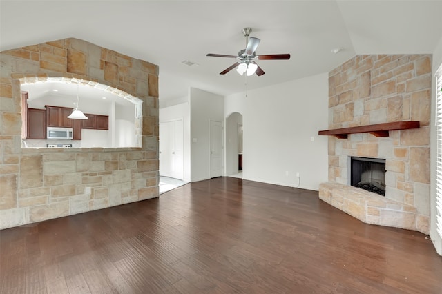 unfurnished living room featuring dark hardwood / wood-style floors, ceiling fan, a stone fireplace, and lofted ceiling