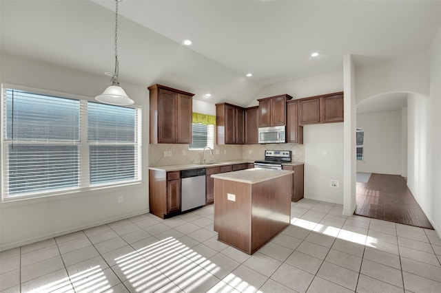 kitchen with vaulted ceiling, light tile patterned floors, appliances with stainless steel finishes, decorative light fixtures, and a kitchen island