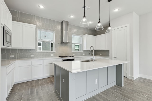 kitchen featuring a center island with sink, white cabinetry, wall chimney range hood, and stainless steel appliances