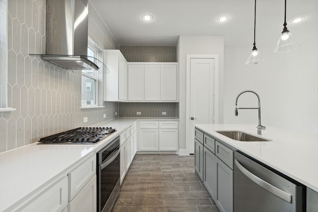 kitchen with white cabinets, wall chimney range hood, hanging light fixtures, sink, and appliances with stainless steel finishes