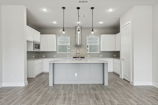 kitchen featuring white cabinetry, stainless steel microwave, an island with sink, and light hardwood / wood-style floors