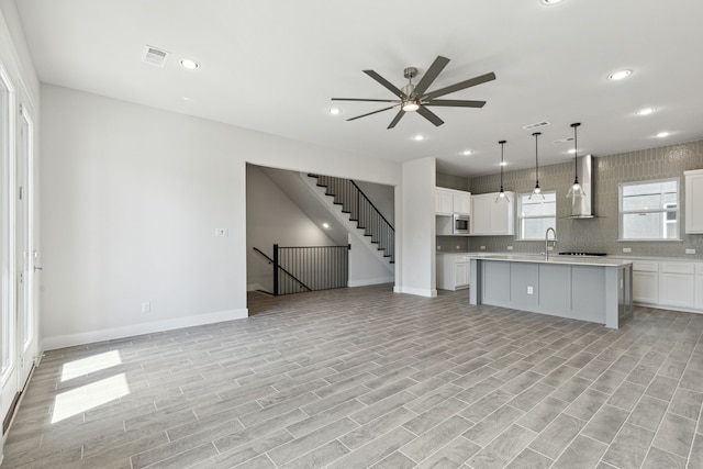 kitchen featuring white cabinetry, a center island with sink, wall chimney exhaust hood, and light wood-type flooring