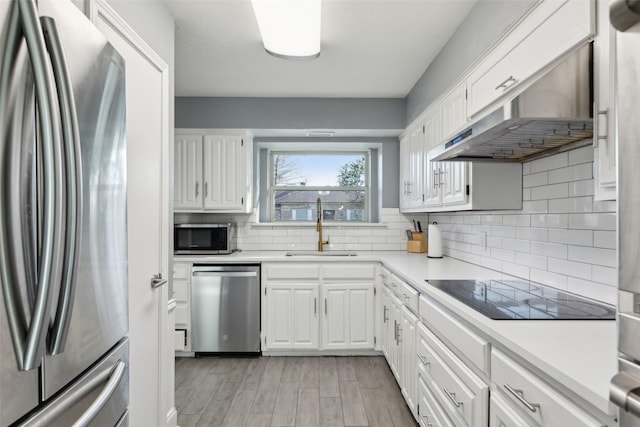 kitchen featuring appliances with stainless steel finishes, exhaust hood, sink, white cabinets, and light hardwood / wood-style floors