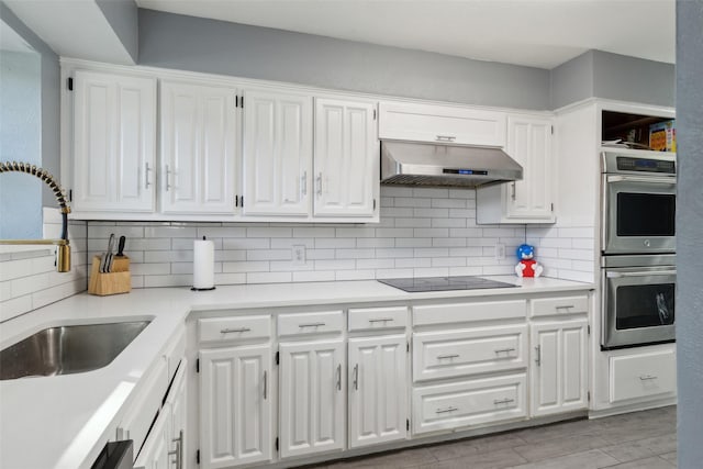 kitchen featuring ventilation hood, sink, stainless steel double oven, black electric cooktop, and white cabinetry