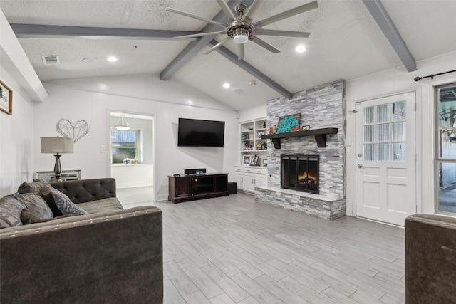 living room featuring light hardwood / wood-style flooring, ceiling fan, lofted ceiling with beams, a textured ceiling, and a stone fireplace